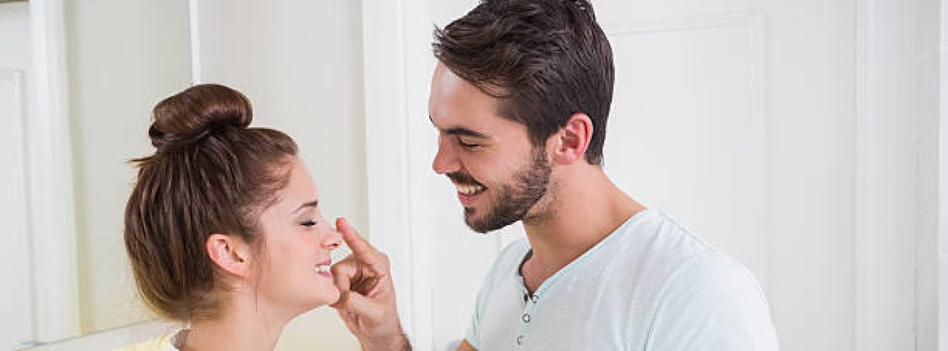 Young man putting cream on girlfriends nose at home in the bathroom