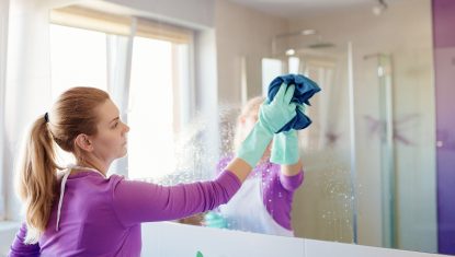 Young beautiful woman in cleaning mirror in bathroom