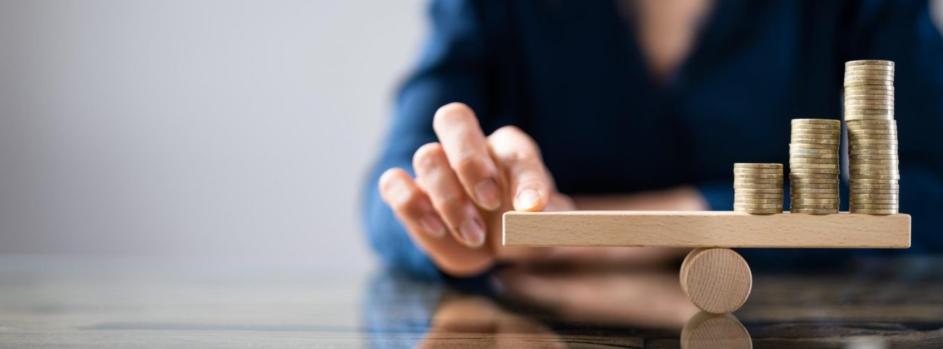 Businessperson Balancing Stacked Coins On Seesaw