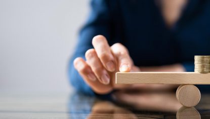 Businessperson Balancing Stacked Coins On Seesaw