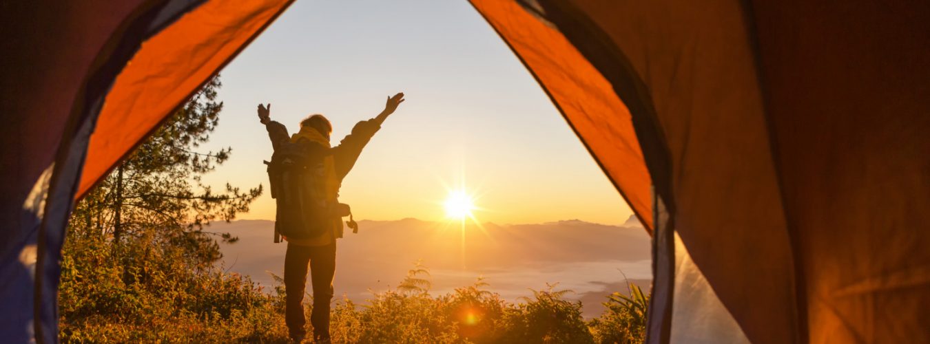 randonneur-debout-devant-tente-orange-devant-camping-sac-dos-montagne