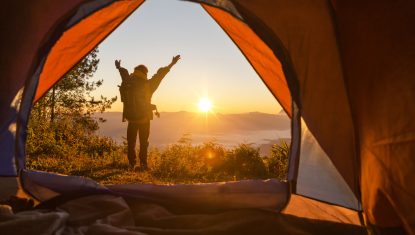 randonneur-debout-devant-tente-orange-devant-camping-sac-dos-montagne