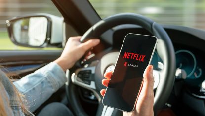 AACHEN, GERMANY – 31. August 2019 : Netflix app on Apple iPhone in car. Young man is browsing the movie video library what to watch.