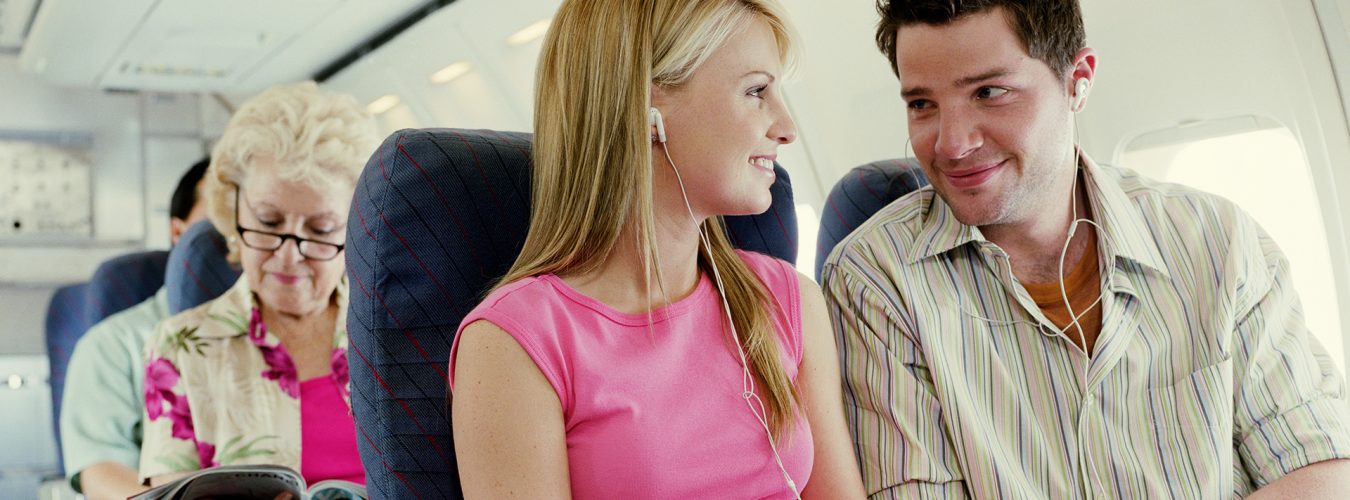 Couple sitting on plane wearing MP3 players, smiling