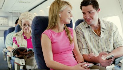 Couple sitting on plane wearing MP3 players, smiling